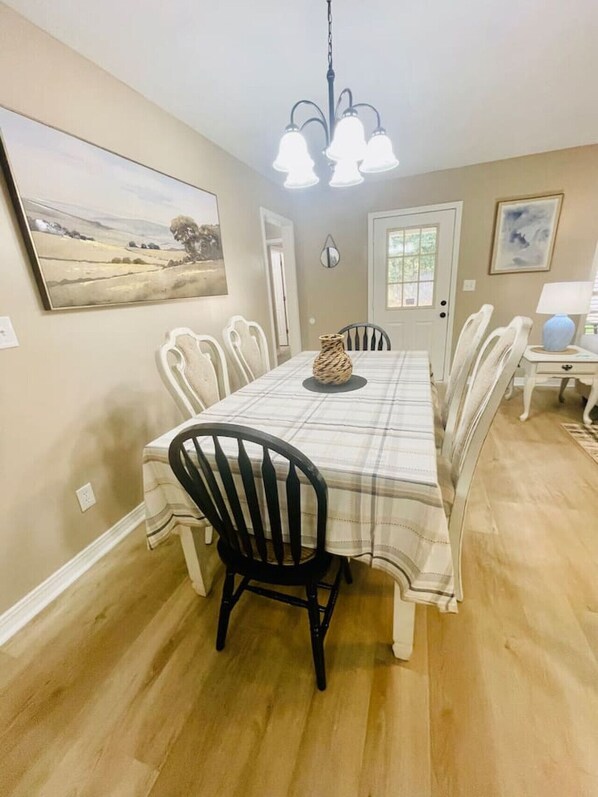 A dining room with a table set for four, surrounded by chairs, a chandelier, and artwork on the walls.