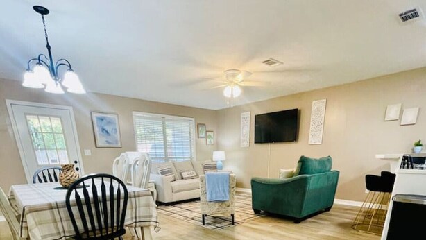 A spacious living area with a dining table, chairs, a sofa, and a TV mounted on the wall.