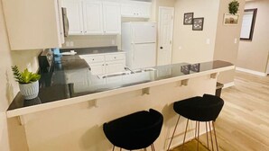 A modern kitchen with white cabinets, a black countertop, and two black bar stools.