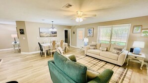 A spacious living room with a green armchair, a beige sofa, and a dining area with a table and chairs.