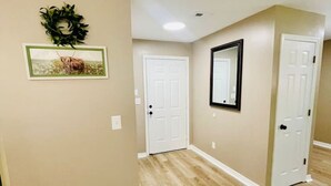 A hallway with beige walls, a wooden floor, and white doors. There is a framed picture and a mirror on the walls.
