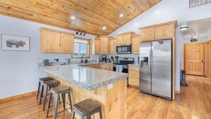 Una cocina con gabinetes de madera, encimera de granito, electrodomésticos de acero inoxidable y techo de madera.
