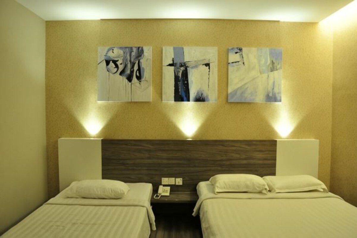 A hotel room with two beds, a wooden headboard, and three wall-mounted paintings.
