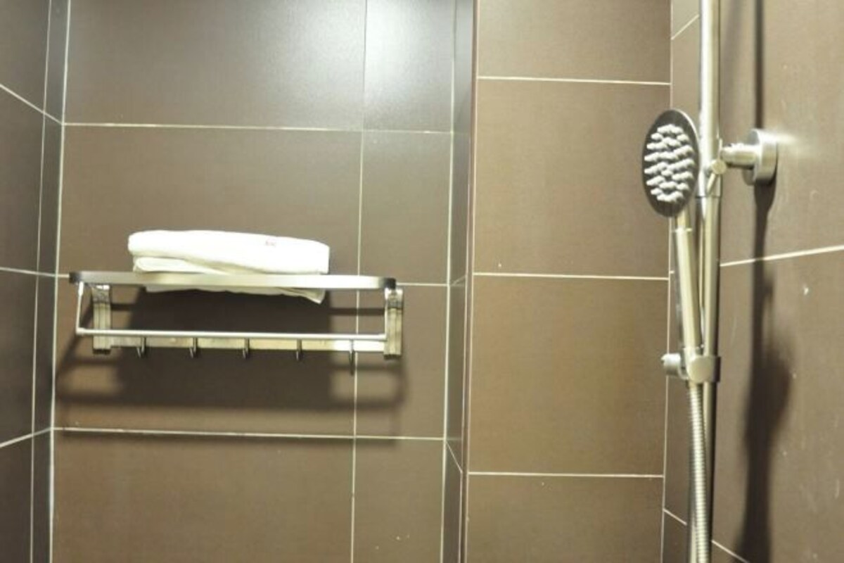 A shower area with a handheld showerhead, a white towel on a rack, and a tiled wall.