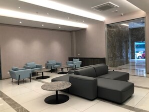 A modern lobby with grey sofas, round tables, and a marble reception desk. - Frazel Inn (Parit Buntar)
