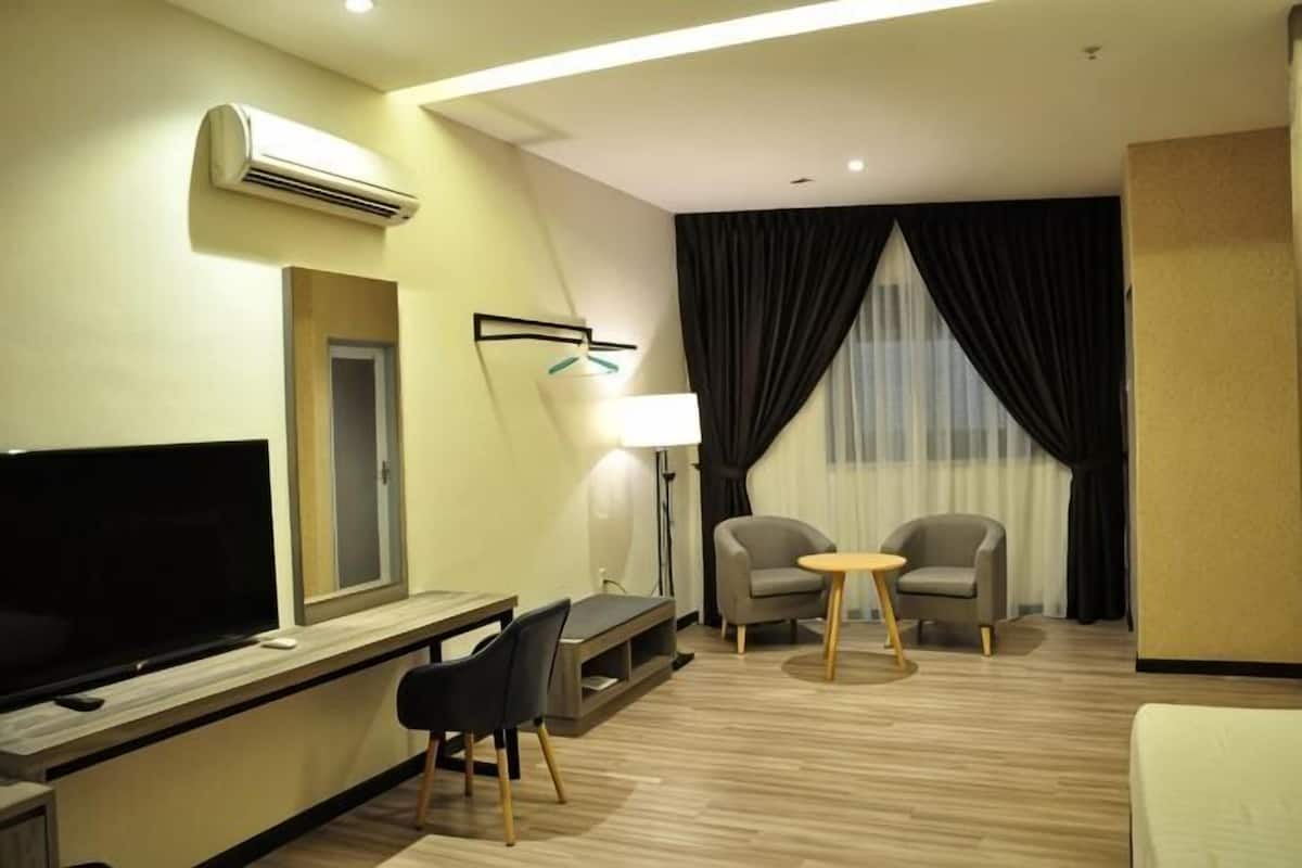 A hotel room with a flat-screen TV, a desk, two chairs, a small table, and a large window with curtains.
