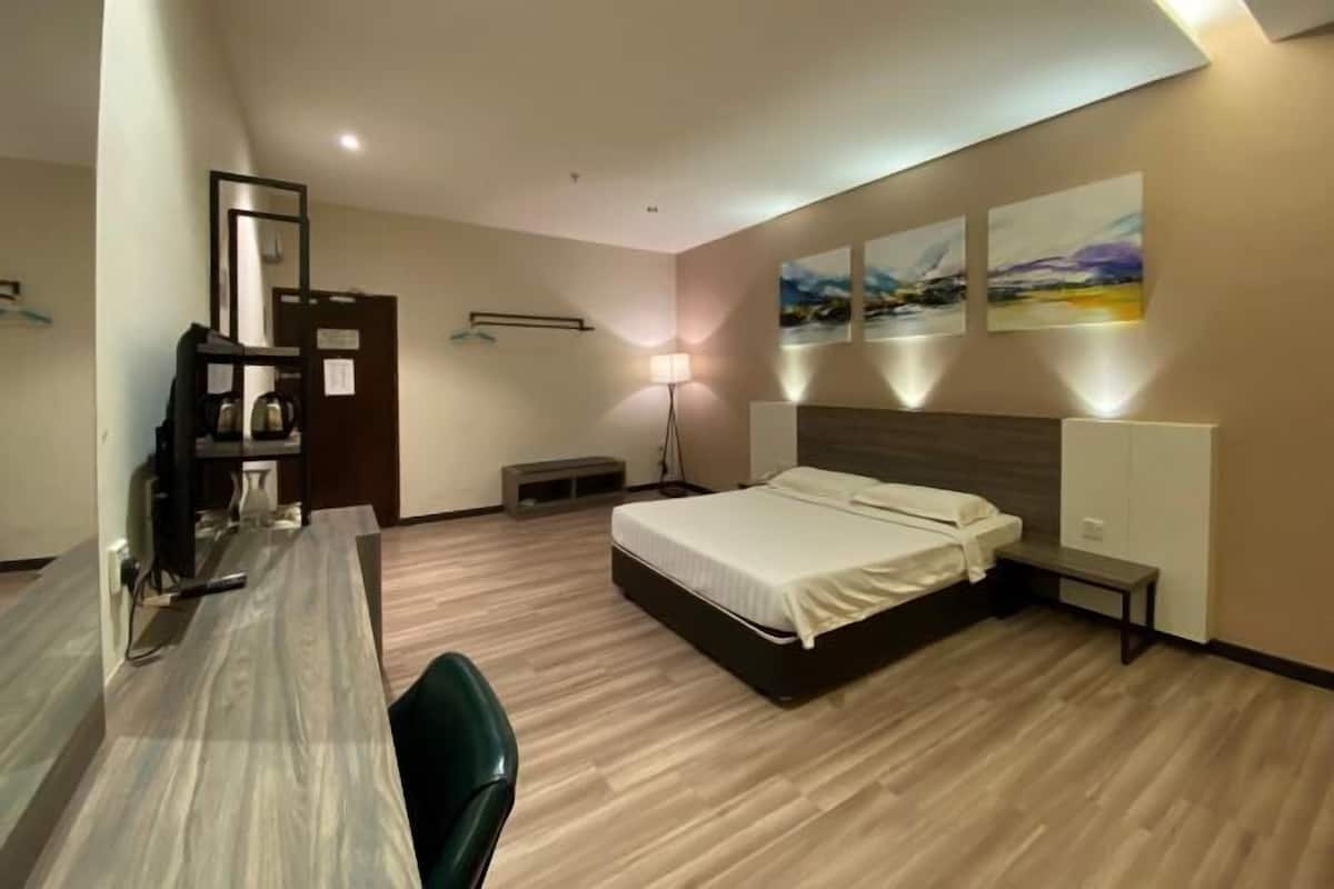 A hotel room with a bed, desk, chair, lamp, artwork, and a small bench.