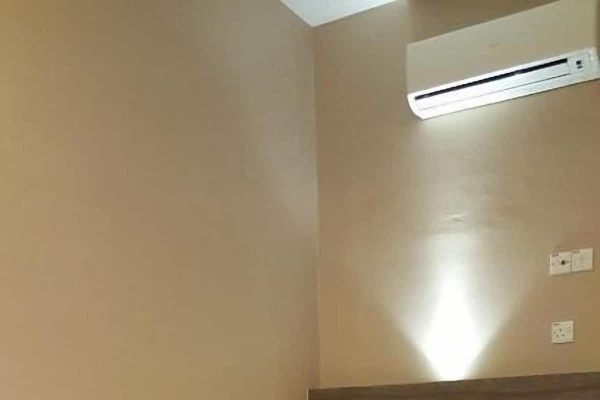 A single bed with a wooden headboard, a wall-mounted air conditioner, and a light switch.