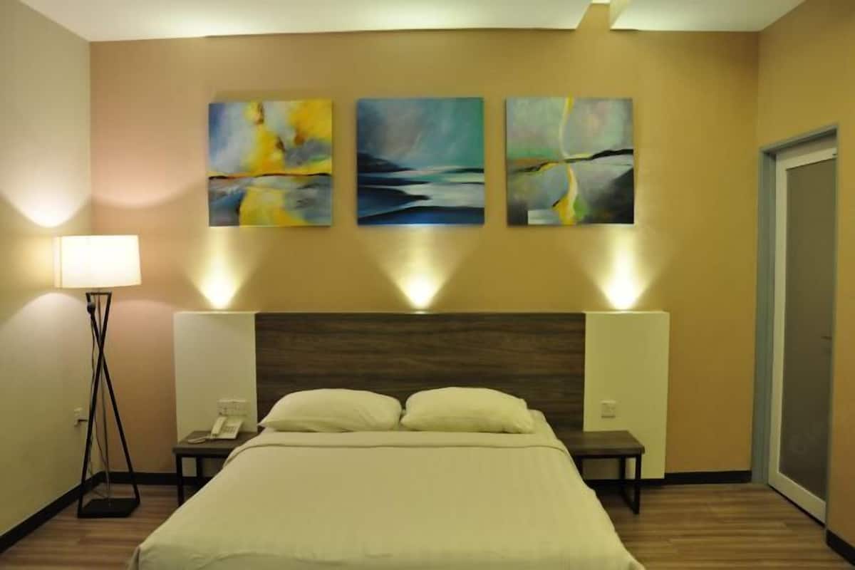 A hotel room with a bed, bedside tables, a lamp, and three abstract paintings on the wall.