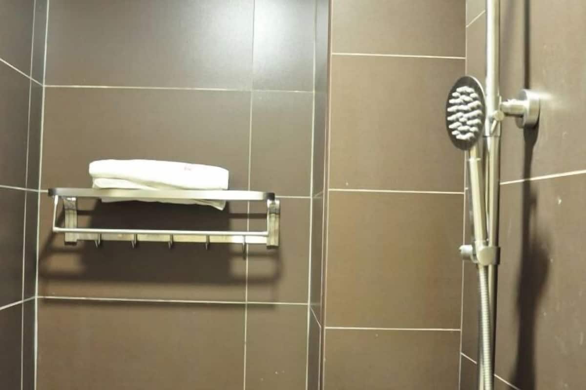 A shower area with a handheld showerhead, a white towel on a rack, and a tiled wall.