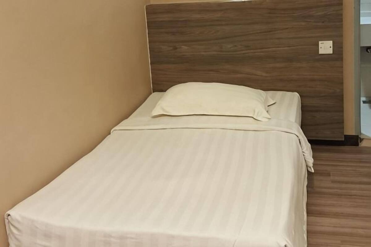 A single bed with a wooden headboard, a plain white bedspread, and a white pillow.