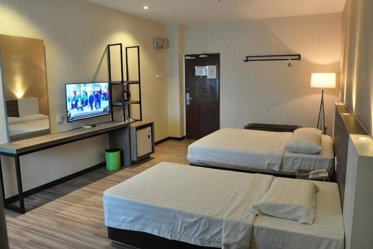 A hotel room with two beds, a TV, a desk, and a lamp.