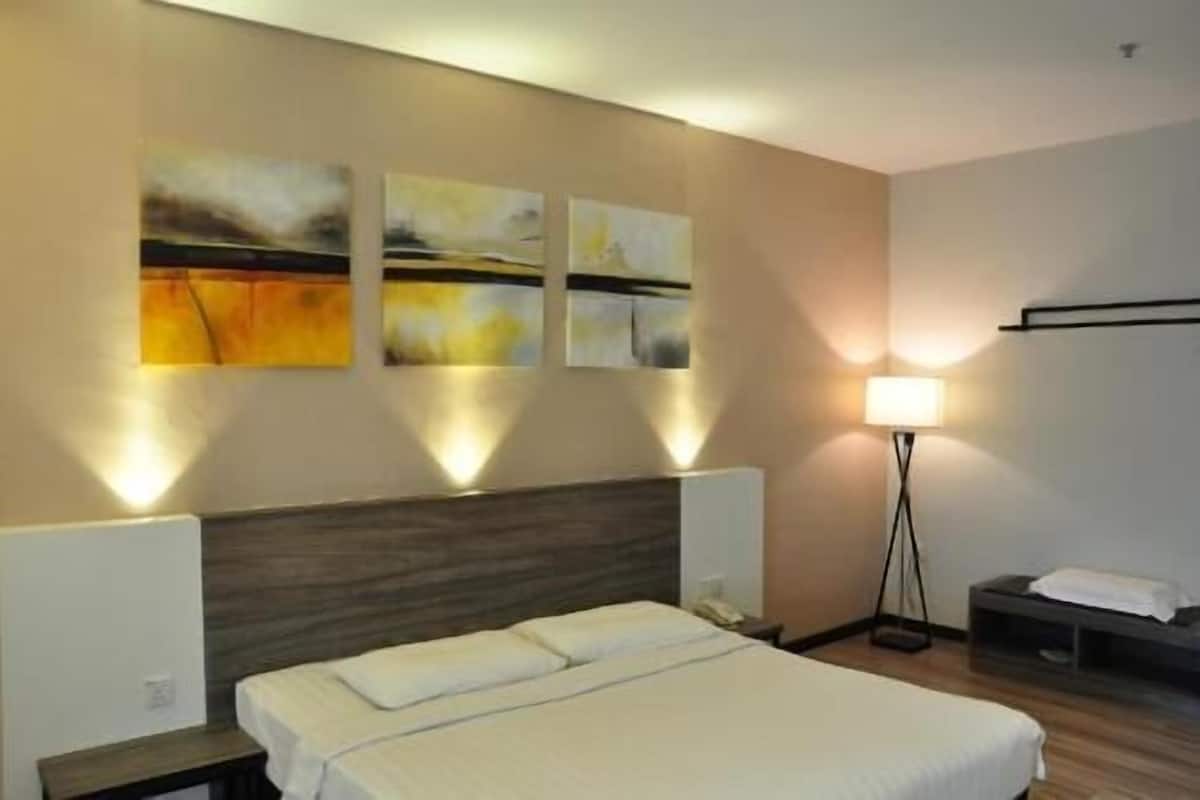 A hotel room with a bed, bedside tables, a lamp, and wall art.