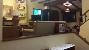 A cozy living room with a sofa, a table with a bottle and glasses, a radiator, and a mirror reflecting the room.