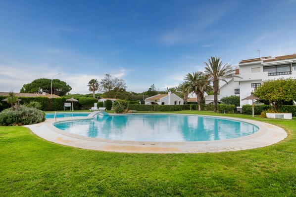 A swimming pool surrounded by a well-maintained lawn, with a clear blue sky above.