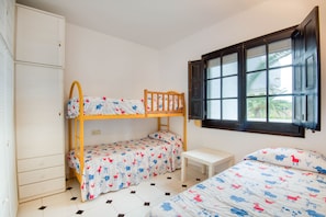 A bedroom with a bunk bed, a single bed, a small table, and a wardrobe.
