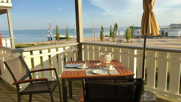 Une terrasse en bois avec une table dressée pour deux personnes, donnant sur une étendue d’eau.