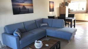 Un salon moderne avec un canapé bleu, une table basse et un tableau représentant un coucher de soleil sur l’eau.