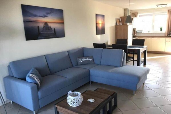 A modern living room with a blue sofa, a coffee table, and a painting of a sunset over water.