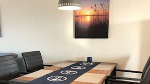 Un espace repas comprenant une table, des chaises, un luminaire suspendu et un tableau accroché au mur.
