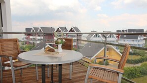 Un balcón con una mesa redonda y dos sillas de madera, con vista a una zona residencial con casas y un cielo despejado.