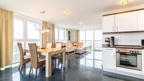 A modern kitchen with white cabinets, a built-in oven, and a dining area with a table and chairs.