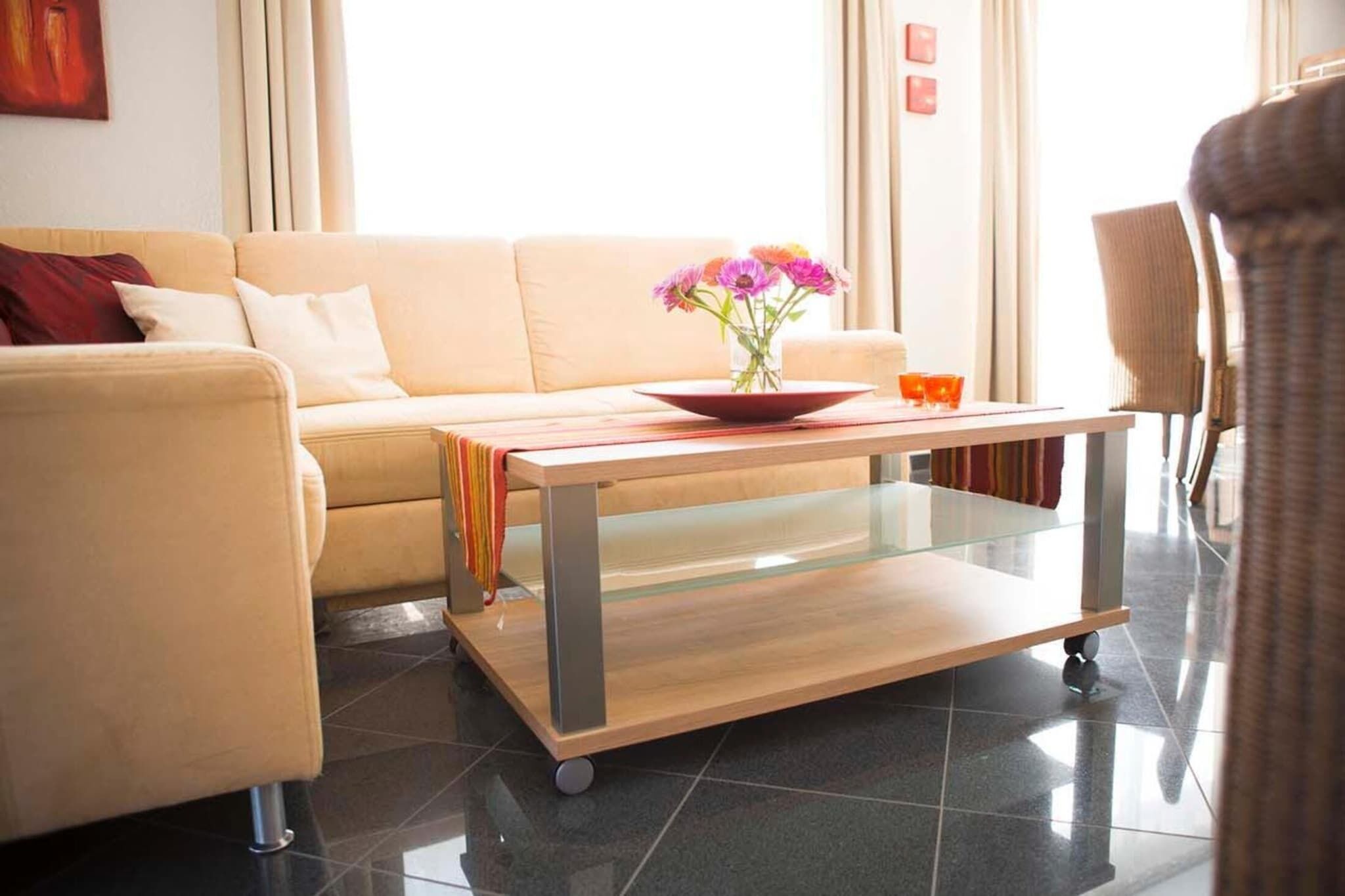 Una sala de estar moderna con un sofá, una mesa de centro de vidrio y un florero con flores.