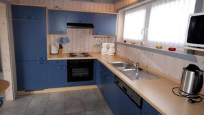 Une cuisine avec des meubles de rangement bleus, une cuisinière, un évier et une fenêtre avec des rideaux.