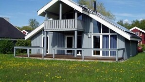 Une maison moderne à deux étages, dotée d’un balcon, de grandes fenêtres et d’un toit en pente.