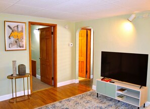 Un salon avec un téléviseur à écran plat posé sur un meuble, une petite table sur laquelle se trouve un vase, et un tapis.
