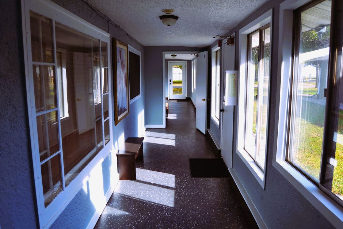 A hallway with large windows, a bench, and a door at the end.