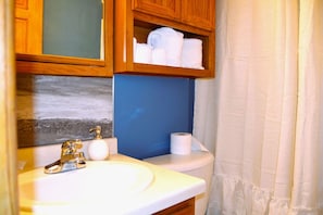 A bathroom with a sink, toilet, and a shelf above the toilet holding towels.