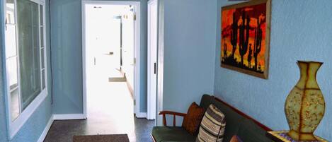 A hallway with a green sofa, a patterned rug, and a vase on a side table.