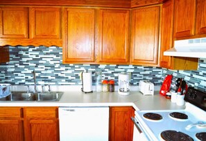 A kitchen with wooden cabinets, a tiled backsplash, a stainless steel sink, a stove, and various kitchen appliances.