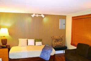 Un dormitorio con cama, mesita de noche, lámpara y una ventana con persianas.