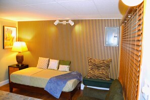 Un dormitorio con cama, mesita de noche, lámpara y ventana con persianas.