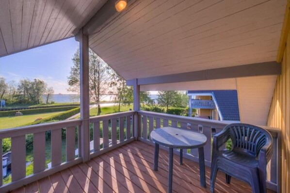 A wooden deck with a table and chairs, overlooking a landscaped garden and a body of water.