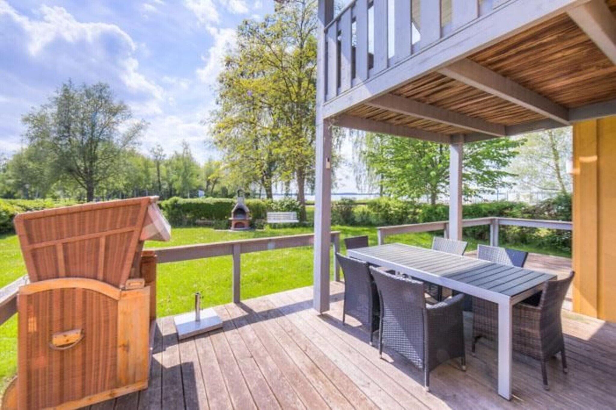 Une terrasse en bois, dotée de mobilier d’extérieur et offrant une vue sur un jardin aménagé.