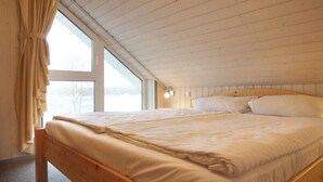 A bedroom with a wooden bed, a window with curtains, and a sloped ceiling.