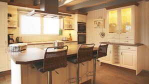 A modern kitchen with a central island, bar stools, white cabinetry, and a built-in oven.