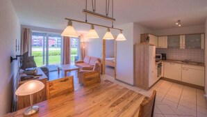 A modern kitchen with wooden cabinets, a dining area with a wooden table and chairs, and a large window providing a view of the outdoors.
