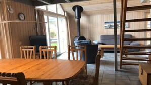 Een houten interieur met een eettafel, stoelen, een bank en een open haard.