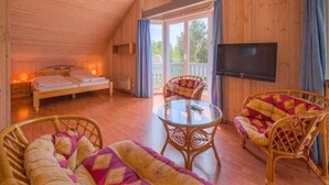 Een gezellig houten huisje met een bed, twee rieten stoelen, een glazen tafel en een televisie.