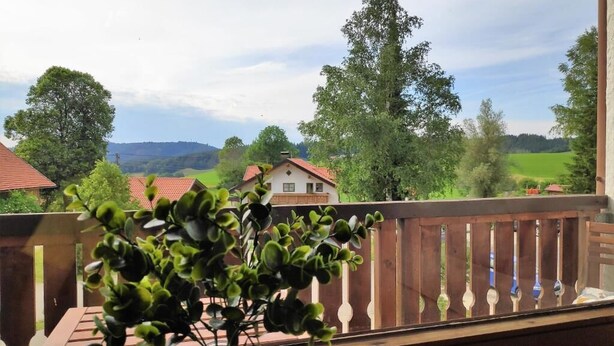 A balcony with a view of a rural landscape, including houses and trees.