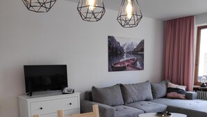 A modern living room with a dining area, a sofa, a TV, and three pendant lights.