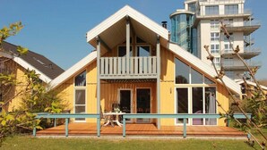 Una casa amarilla con balcón, terraza de madera y cielo azul despejado.