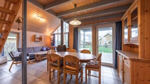 Un interior de madera con una mesa de comedor, sillas y un sofá. Hay ventanas amplias y vistas al exterior.