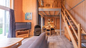 A cozy cabin interior with a wooden interior, a fireplace, a dining area, and a staircase leading to a loft. - exklusives skandinavisches Ferienhaus (Rechlin)