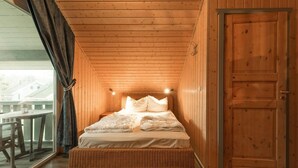 A wooden-paneled room with a bed, a window with curtains, and a door. - exklusives skandinavisches Ferienhaus (Rechlin)