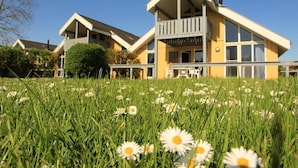 A two-story house with a balcony, surrounded by a grassy field with daisies. - exklusives skandinavisches Ferienhaus (Rechlin)